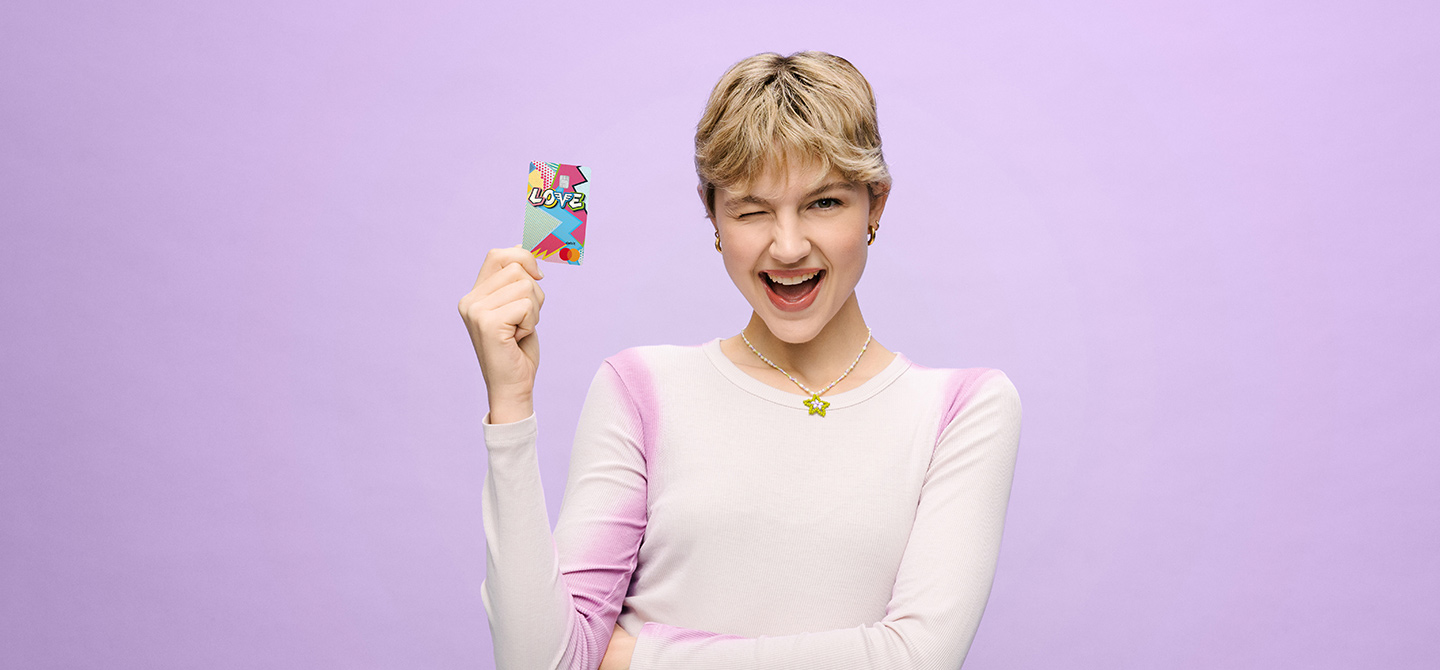 Eine junge Frau mit kurzen, blonden Haaren hält lächelnd eine Jugendkarte der Volksbanken in der Hand.